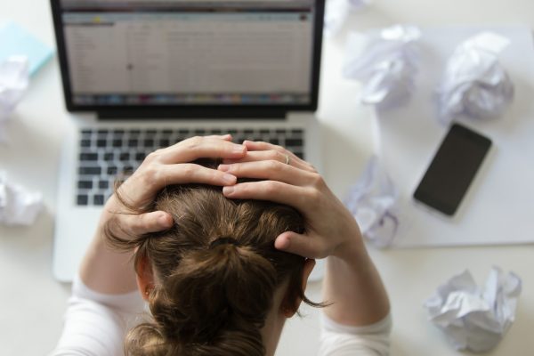 Top view portrait of a woman grabbing her head in despair at the desk near the laptop. Education, business concept photo. Lifestyle